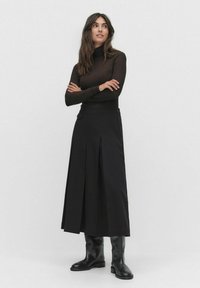 Czarna plisowana spódnica midi wykonana z gładkiego materiału. W połączeniu z dopasowanym, długim brązowym golfem i czarnymi botkami do kolan.