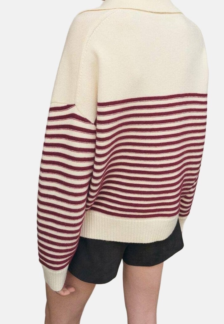 Personne portant un pull crème avec des rayures horizontales bordeaux sur les manches et le torse, associée à un short noir, vue de dos.