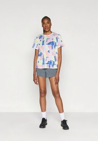 T-shirt de manga curta com estampado gráfico apresentando padrões abstratos multicoloridos; combinada com calções cinzentos e sapatilhas pretas com meias brancas.