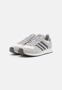Pair of gray and white Adidas sneakers with black stripes, laces, and textured white midsoles on a white background.