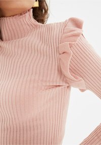 Top a coste rosa chiaro con collo alto e dettagli arricciati sulle spalle, che mette in evidenza un tessuto testurizzato e un design aderente.