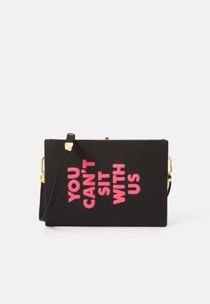 Sac en bandoulière en tissu noir avec un texte brodé rose disant "TU NE PEUX PAS T'ASSEOIR AVEC NOUS", doté d'un fermoir doré et d'une bandoulière réglable.