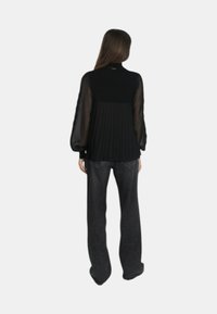 Top nero con maniche a palloncino trasparenti e dettaglio plissettato sul retro, abbinato a pantaloni scuri a gamba larga. Design semplice ed elegante.