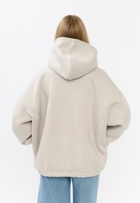 Przeciętny kremowy hoodie z dużym kapturem, opadającymi ramionami, ściągaczem u dołu i gładką teksturą, w zestawieniu z jasnoniebieskimi spodniami typu straight-leg.