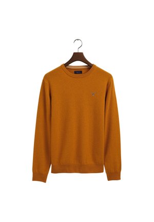 Brązowo-pomarańczowy sweter z długim rękawem i okrągłym dekoltem, z prążkowanymi mankietami i obszyciem, wiszący na ciemnym drewnianym wieszaku na białym tle.