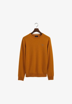 Pull à col rond, manches longues, couleur orange brunâtre, avec poignets et ourlet côtelés, suspendu à un cintre en bois foncé sur un fond blanc.