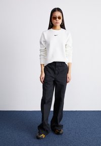 Λευκή φούτερ μπλούζα με μαύρο λογότυπο Nike, μαύρο παντελόνι και μαύρα παπούτσια με κίτρινες λεπτομέρειες. Γυαλιά ηλίου και κρίκοι ολοκληρώνουν την εμφάνιση.