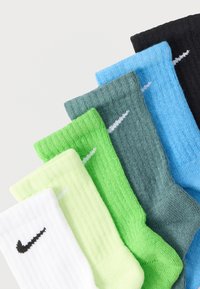Χρωματιστή συλλογή κάλτσες Nike: λευκές, νέον κίτρινες, πράσινες, τιρκουάζ και μαύρες· ριγέ υφή με μικρό μαύρο λογότυπο σε κάθε μία.