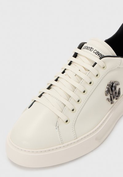 Fehér fűzős sportcipő fekete bélésrésszel, ezüst kígyólogóval az oldalon és "roberto cavalli" felirattal a nyelvén.
