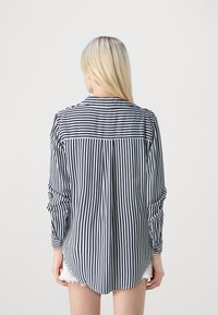Camisa de manga larga, con botones, rayas verticales en azul marino y blanco, con un dobladillo curvado, plisado en la parte posterior y puños remangados.