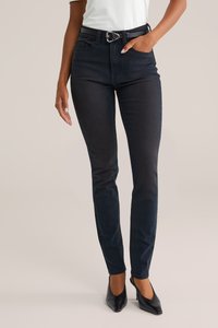 Melnas šauras bikses ar gludu tekstūru, ar augstu vidukli, jostu cilpām un elegantu jostasvietu. Apvienotas ar melniem papēža apaviem.