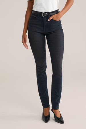 Čierne úzke džínsy s hladkou textúrou, s vyšším pásom, pútkami na opasok a elegantným pásom. Spárované s čiernymi topánkami na podpätku.