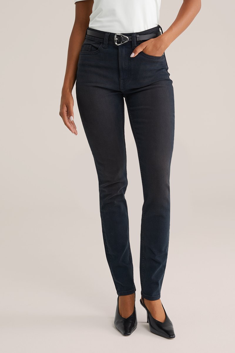 Crne skinny traperice glatke teksture, s visokim strukom, petljama za remen i elegantnim pojasom. Uparene s crnim cipelama na petu.