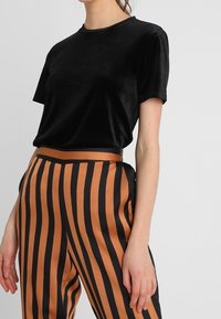 Černé sametové tričko s krátkým rukávem v kombinaci s kalhotami s vysokým pasem, které mají černé a měděné svislé pruhy. Hladká textura.