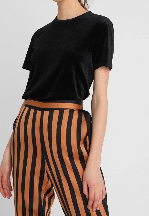 Černé sametové tričko s krátkým rukávem v kombinaci s kalhotami s vysokým pasem, které mají černé a měděné svislé pruhy. Hladká textura.