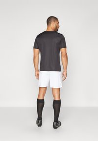 Maglietta sportiva nera, pantaloncini bianchi, calze nere fino al ginocchio. Maniche corte, design aderente, texture liscia e dettagli a contrasto.