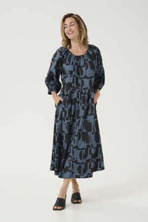 Long-sleeve, loose-fit dress featuring a blue and black abstract pattern, elastic waist, and soft fabric. Worn with open-toe black shoes.