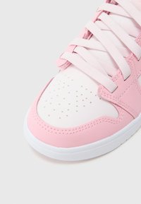 Rózsaszín sportcipő sima bőrfelsőrésszel, fehér perforált orr-résszel, fehér talppal, valamint hozzáillő cipőfűzőkkel és varrási részletekkel.