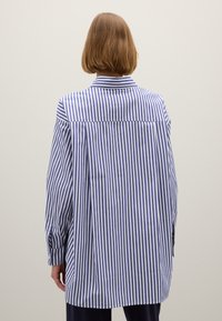 Losse button-up shirt met blauw-witte verticale strepen, lange mouwen met knoopsluiting en een achteropening voor extra bewegingsvrijheid.