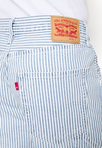 Närbild av blå och vita randiga Levi's-jeans baksida ficka med röd Levi's-flik och lädermärkesetikett som visar storlek W31 L.