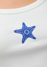 Witte ribstof met een blauw geborduurde zeesterontwerp met gedetailleerde lijnen en een cirkelvormige accent in het midden.