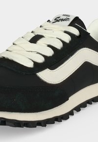 Ασπρόμαυρο αθλητικό παπούτσι Vans Serio με λευκά κορδόνια, κυματιστή πλευρική ρίγα και ανάγλυφη μαύρη σόλα.