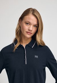 Granatowa koszulka polo z długim rękawem, z różowym wykończeniem kołnierza, z zapięciem na guziki oraz małym logo "POLO CLUB" na lewej piersi.