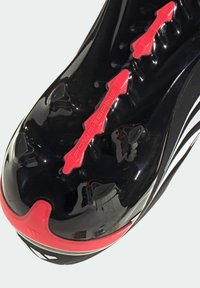 Μαύρη σόλα παπουτσιού ποδοσφαίρου με υφή, κόκκινη διακοσμητική λεπτομέρεια "POWERSPINE" και μαύρα καρφιά για πρόσφυση. Λεία επιφάνεια με λευκή ρίγα.