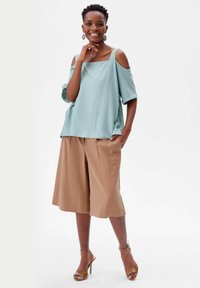 Jasnoniebieska bluzka off-shoulder z koronkowymi akcentami, w połączeniu z beżowymi szerokimi spodniami culottes i brązowymi sandałami na obcasie. Gładki materiał, luźny krój.