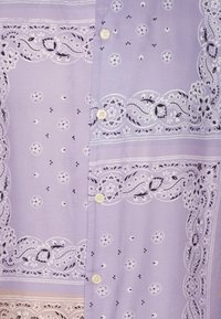 Světle fialová blůza s propracovanými bílými květinovými a paisley motivy, s knoflíky a jemnou texturou.