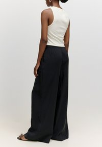 Schwarze weit geschnittene Hose mit einer glatten Textur, hohem Bund und Falten, kombiniert mit einem enganliegenden, ärmellosen Top in Creme. Schlichtes, modernes Design.
