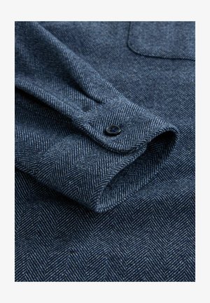 Dunkelblaues Fischgrätmuster am Hemdärmel, mit glatter Textur, einem einzelnen Knopfverschluss und sichtbaren Nähten auf dem Stoff.