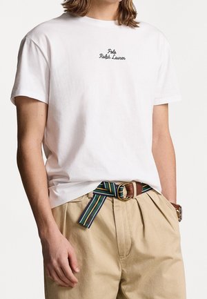 Biała koszulka z czarnym haftem "Polo Ralph Lauren" na piersi, zestawiona z khaki spodniami i wielokolorowym paskiem w paski z brązową klamrą.