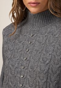 Pulover gri tricotat, cu un guler înalt cu nervuri, model texturat din cabluri și nasturi decorativi pe partea din față pentru un plus de detaliu.