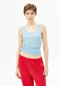 Hellblaues Tanktop mit enger Passform, am Taillenbereich geknotet, kombiniert mit roten Sweatpants mit elastischem Bund und Logodetail.