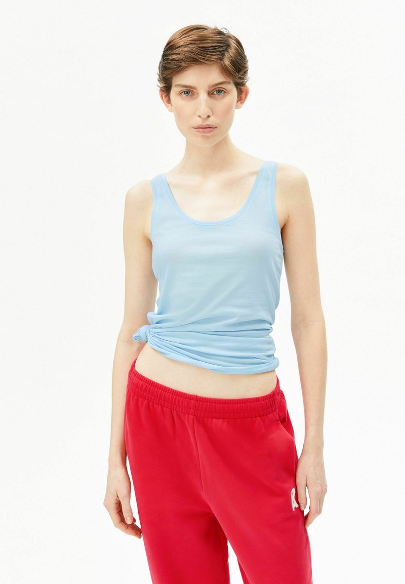 Hellblaues Tanktop mit enger Passform, am Taillenbereich geknotet, kombiniert mit roten Sweatpants mit elastischem Bund und Logodetail.