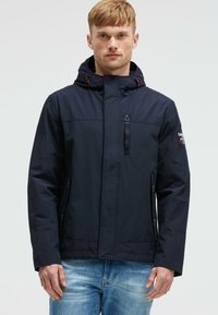 Granatowa wodoodporna kurtka z kapturem, przednim zamkiem i bocznymi kieszeniami. Posiada czerwone akcenty i gładką fakturę, odpowiednia do użytku na zewnątrz.