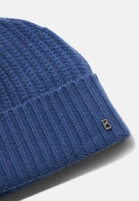 Niebieska dziana czapka beanie z teksturowaną górną częścią i prążkowanym dolnym odcinkiem. Posiada srebrny akcent logo po boku. Wykonana z miękkiego materiału wełnianego.