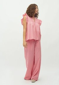 Completo due pezzi rosa con top a maniche voluminose e pantaloni larghi con una trama a righe. Tessuto leggero e silhouette comoda.