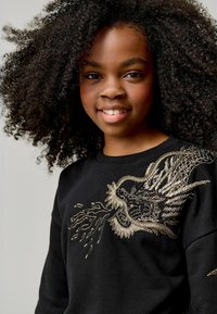 Sudadera negra con un diseño de dragón bordado en oro con textura en la parte frontal. Tejido suave con cuello redondo y mangas largas.