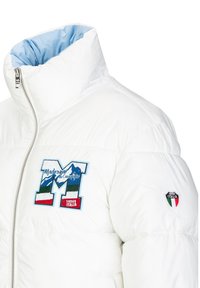 Weißer Daunenjacke mit hohem Kragen, ausgestattet mit hellblauem Innenfutter. Auffälliges gesticktes Logo mit Bergen, den Farben Italiens und dem Jahr 1969.
