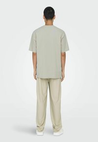 Lichtgrijze, oversized t-shirt met korte mouwen en een ronde hals, afgewerkt met losse beige broek. Effen stof met minimale ontwerpdetails.