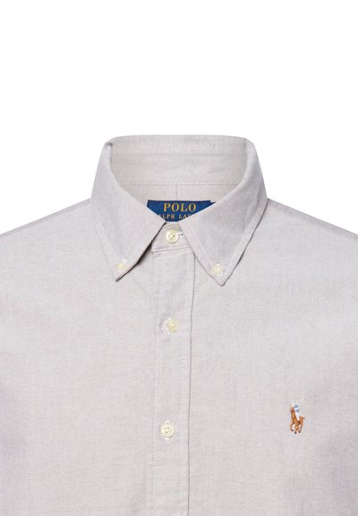 Chemise boutonnière gris clair avec un col classique, dotée d'un petit logo brodé sur la poitrine gauche et de boutons blancs.