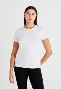 Hvit bomulls t-skjorte med korte ermer, rund hals og glatt tekstur, parret med svarte leggings. Ingen synlige mønstre eller dekorasjoner.