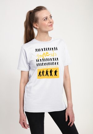 Młoda kobieta w białej koszulce z czarnymi sylwetkami chodzących postaci, żółtym napisem "Genesis" oraz grafiką o tematyce koncertowej.