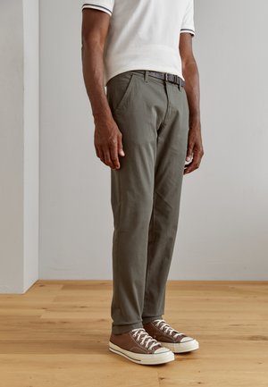 Khaki cotton trousers with tailored fit, side pockets, worn with brown sneakers featuring white soles and laces. Simple, clean design.