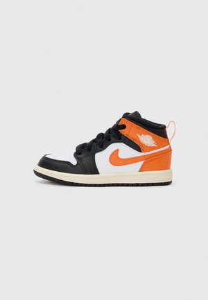 Wysokie buty sportowe w czerni, bieli i pomarańczy z czarnymi sznurowadłami i białą podeszwą, z widocznym logo Nike swoosh i Air Jordan.