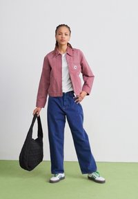 Roze canvasjack met een voorzak, witte t-shirt, blauwe losse denim broek, zwarte gewatteerde tote bag en sneakers met groene accenten.