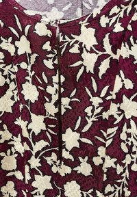 Robe florale bordeaux avec des motifs crème, présentant un tissu texturé, un col rond et un détail de fermeture verticale.