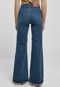 High-waisted flared jeans in donkerblauwe denim, met een leren logo-patch op de achterkant, een gladde textuur en brede broekspijpen.